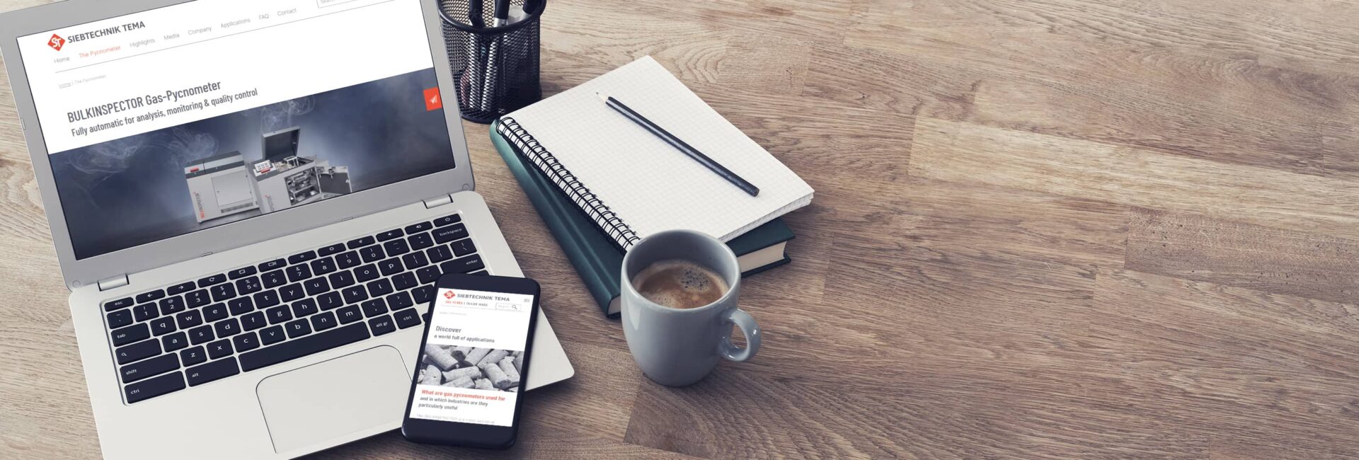 Ein Tisch mit Kaffee, einigen Stiften, Papier, einem Laptop und einem Smartphone, auf dem die neue BULKINSPECTOR Website zu sehen ist.